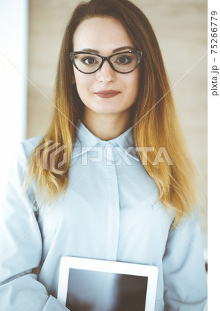 Business woman headshot at workplace in modern office. Unknown businesswoman standing straight with tablet computer. Young accountant or secretary looks good Business woman headshot at workplace in modern office. Unknown businesswoman standing straight with tablet computer. Young accountant or secretary looks good 75266779