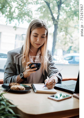 Young girl student sitting in cafe with laptop, smartphone and cup of coffee. Student learning online, distant education, remote freelancer working in coffee shop 75267667