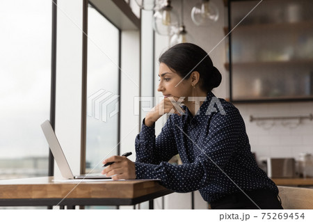 Close up thoughtful Indian businesswoman looking at laptop screen 75269454