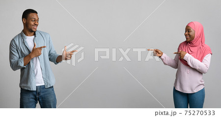 Black man and woman pointing at empty space between them Black man and woman pointing at empty space between them 75270533