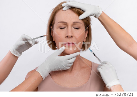 Injection cosmetology for skin rejuvenation. Beauticians making anti-aging shots into mature woman's face 75270721