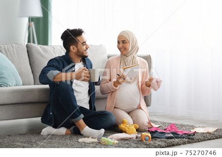 Happy pregnant muslim couple getting geady for childbirth, making checklist at home 75270746