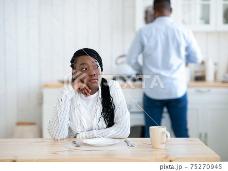 Portrait Of Thoughtful Young Black Woman Sitting At Table In Kitchen Portrait Of Thoughtful Young Black Woman Sitting At Table In Kitchen 75270945
