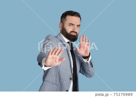 Confident office worker showing STOP gesture with both hands, expressing negative attitude on blue studio background Confident office worker showing STOP gesture with both hands, expressing negative attitude on blue studio background 75270989
