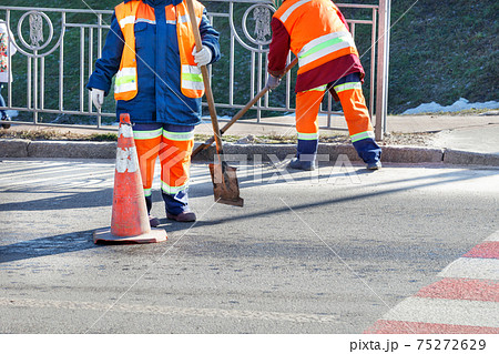 A team of street cleaners sweep the road on a sunny spring day. 75272629