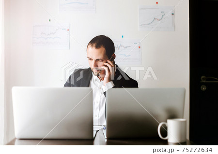smiling businessman talking on phone sitting at desk smiling businessman talking on phone sitting at desk 75272634