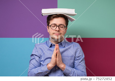 Caucasian smart man with stacks of books on top of his head meditating. Caucasian smart man with stacks of books on top of his head meditating. 75272852