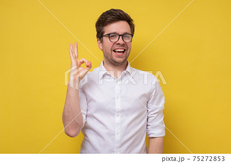Cheerful young man gesturing OK sign on yellow wall. Cheerful young man gesturing OK sign on yellow wall. 75272853