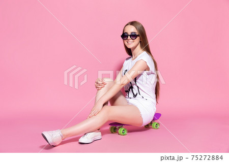 Cheerful young girl with a skateboard on the pink background 75272884