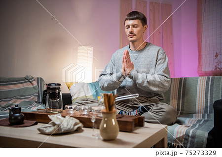 A man meditates to achieve harmony with the world around him, before starting a traditional oriental tea party at the tea table and bamboo tray. 75273329