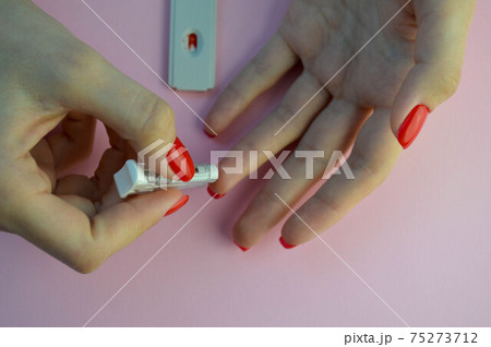 coronavirus test on a pink matte background. medical procedure. the girl pierces her finger with a lancet and adds a drop of blood to the sensitive test strip 75273712