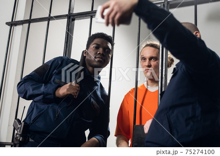 Wardens in a maximum security prison take selfies with a prisoner with tattoos on his face, who is sitting in a cell. Wardens in a maximum security prison take selfies with a prisoner with tattoos on his face, who is sitting in a cell. 75274100