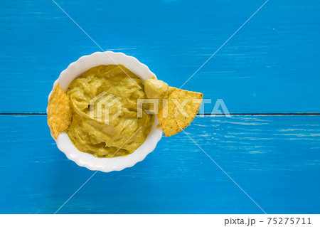 Nachos chips dipping in salsa guacamole over a blue background Nachos chips dipping in salsa guacamole over a blue background 75275711