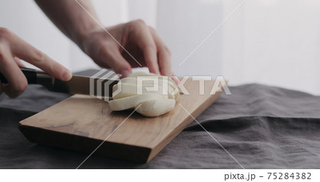 man slicing mozzarella ball on olive wood board with window on background 75284382