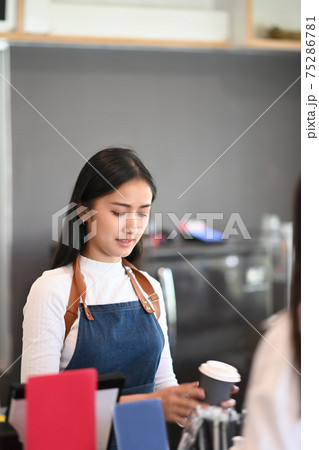 Cheerful barista giving paper cups of coffee to customer at counter bar. Cheerful barista giving paper cups of coffee to customer at counter bar. 75286781