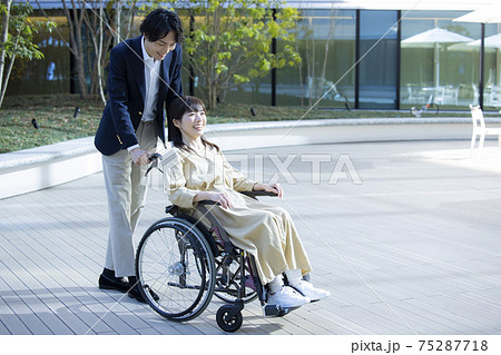 車椅子の女性と介助する男性 75287718