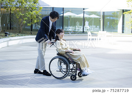 車椅子の女性と介助する男性 75287719