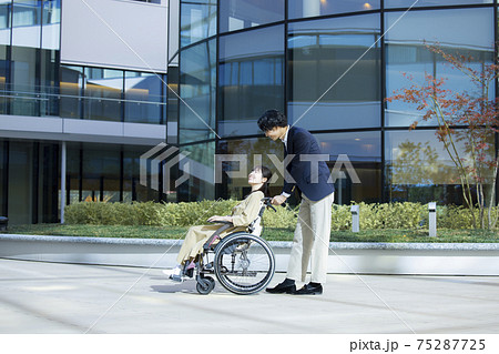 車椅子の女性と介助する男性 75287725