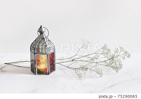 Burning silver vintage Moroccan, Arabic lantern. White gypsophila, babys breath flowers on marble table background. Muslim holiday Ramadan Kareem greeting card, invitation. Empty copy space. 75290065
