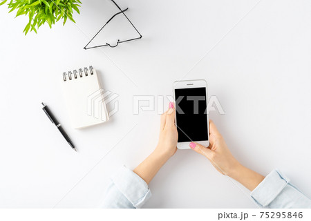 Young woman using mobile phone over white table. Office desktop. Top view Young woman using mobile phone over white table. Office desktop. Top view 75295846