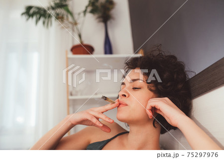 Woman laying on her bed and smoking her hand-rolled cigarette 75297976