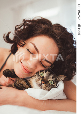 Happy young woman spending time with her cat in bed at home 75298114