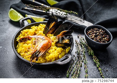 The Spanish Seafood paella in a pan with prawns, shrimps, octopus and mussels. Black background. Top view 75298744
