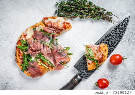 Italian Pizza with parma ham, arugula and cheeseon a kitchen table. White background. Top view Italian Pizza with parma ham, arugula and cheeseon a kitchen table. White background. Top view 75299127