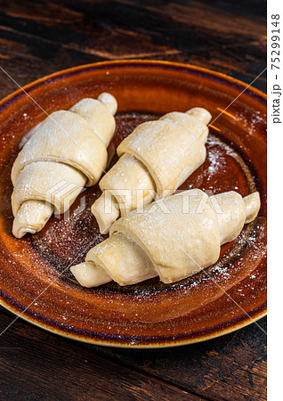 Raw uncooked homemade croissant on a rustic plate. Dark Wooden background. Top view 75299148