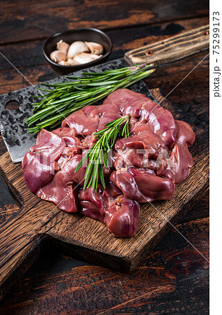Raw liver chicken offals meat on a wooden cutting board with butcher cleaver. Dark wooden background. Top view 75299173