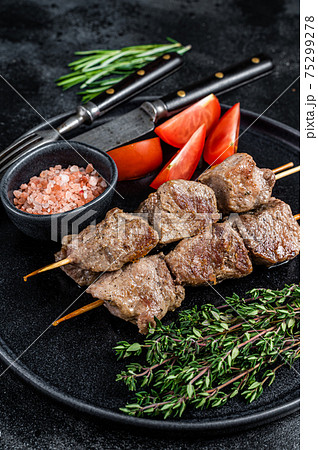 Roasted meat skewers shish kebab and vegetables on a plate. Black background. Top view 75299278