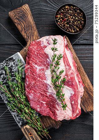 Fresh Raw Round roast beef meat cut on a butcher cutting board with cleaver. Black wooden background. Top view 75299344