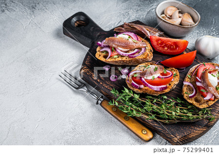Toasts with olive oil, herbs, tomatoes and spicy anchovy fillets. White background. Top view. Copy space 75299401