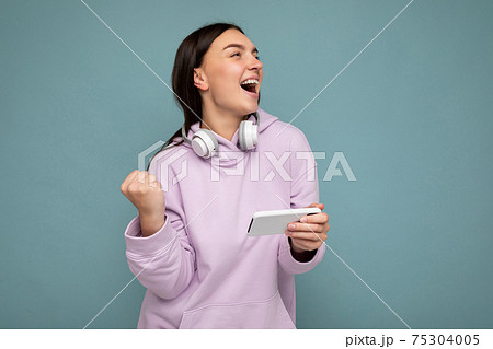 Beautiful happy smiling young brunette female person wearing light purple hoodie isolated over blue Beautiful happy smiling young brunette female person wearing light purple hoodie isolated over blue 75304005