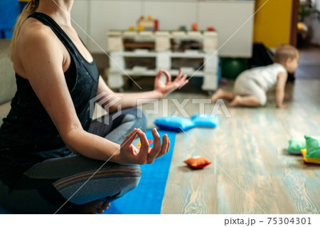 Mindfulness meditation concept. Young woman, mother practicing yoga at home sitting in lotus pose, meditating relaxing with closed eyes with baby daughter at home. Mindfulness meditation concept Mindfulness meditation concept. Young woman, mother practicing yoga at home sitting in lotus pose, meditating relaxing with closed eyes with baby daughter at home. Mindfulness meditation concept 75304301