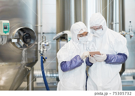 Two Workers Wearing Hazmat Suits Using Tablet Two Workers Wearing Hazmat Suits Using Tablet 75305732