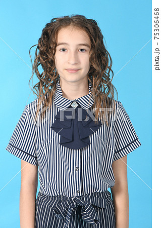 Portrait of adorable smiling schoolgirl with curl hair, standing isolated on a blue background. 75306468