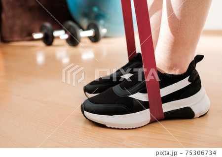 Close up female legs in sneakers doing exercises with fitness elastic bands at home during lockdown. Home workout. with resistances bands. Close up female legs in sneakers doing exercises with fitness elastic bands at home during lockdown. Home workout. with resistances bands. 75306734