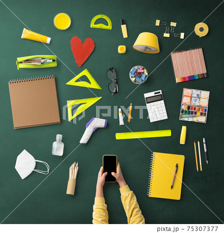 Flat lay top view of child with smartphone and school supplies, distance learning and coronavirus concept. Flat lay top view of child with smartphone and school supplies, distance learning and coronavirus concept. 75307377