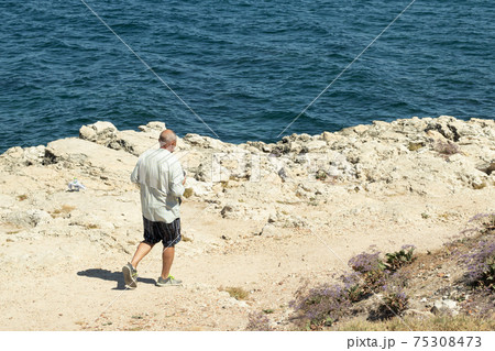 Tourist walks along the sandy path, mountain hiking. Blue sea on background 75308473