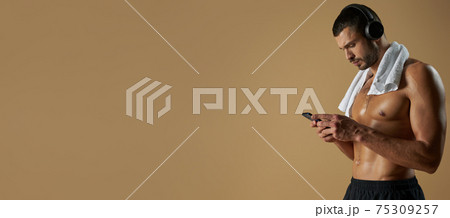 Website header of Focused strong athlete in black sportswear with towel on his shoulder standing in studio with modern device Website header of Focused strong athlete in black sportswear with towel on his shoulder standing in studio with modern device 75309257