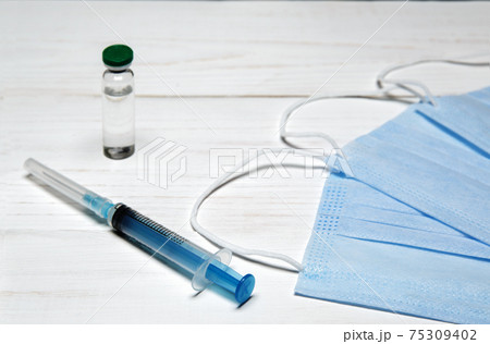 vaccine bottle, injection syringe and medical mask on a white table vaccine bottle, injection syringe and medical mask on a white table 75309402