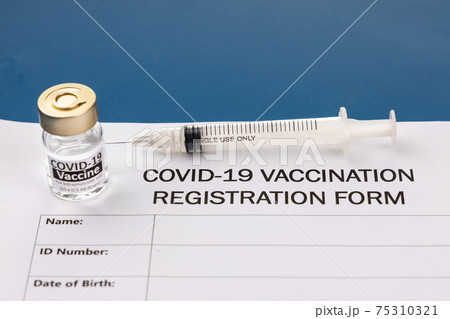 Covid-19 vaccination registration form with vial and syringe on blue desk Covid-19 vaccination registration form with vial and syringe on blue desk 75310321