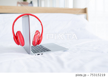 Red color music headphone with laptop computer on white bed 75315219