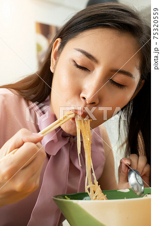 Woman eats spicy hot tomyum noodle soup and hanging on chopstick Woman eats spicy hot tomyum noodle soup and hanging on chopstick 75320559