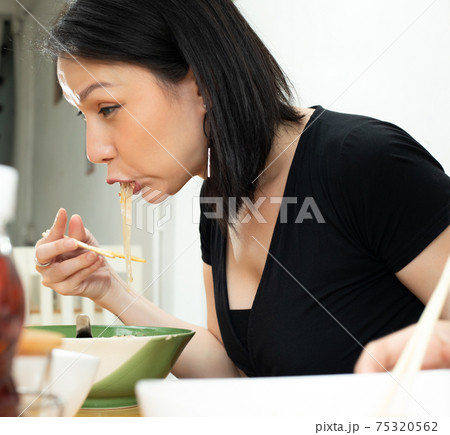 Woman eats spicy hot tomyum noodle soup and hanging on chopstick 75320562