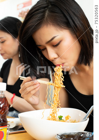 Woman eats spicy hot tomyum noodle soup and hanging on chopstick 75320563