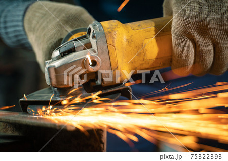 Locksmith in special clothes and goggles works in production. Metal processing with angle grinder. Sparks in metalworking Locksmith in special clothes and goggles works in production. Metal processing with angle grinder. Sparks in metalworking 75322393