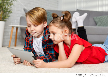 cute brother and sister with tablet lying on floor at home 75323420