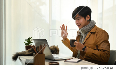Asian man having video call on laptop computer and greeting his colleagues. Asian man having video call on laptop computer and greeting his colleagues. 75325038